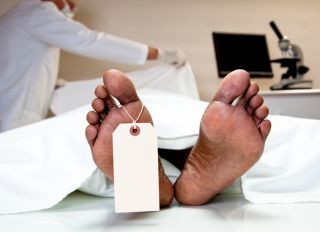 Mortician, coroner covering dead body in morgue. Feet, toe tag.