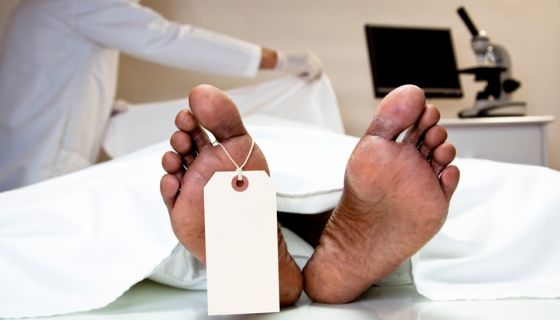 Mortician, coroner covering dead body in morgue. Feet, toe tag.