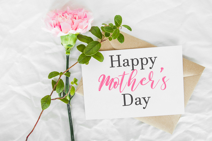 craft envelope, white sheet of paper, one pink carnation and green leaves, inscription text happy mother s day, holiday and sweet wishes concept