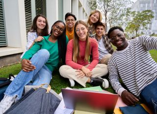 Portrait of a large group multiracial friends sitting posing smiling with laptop and workbooks