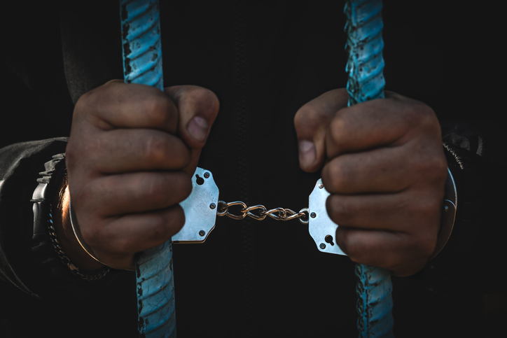 concept of unfreedom. cropped image of african american prisoner in handcuffs behind prison bars