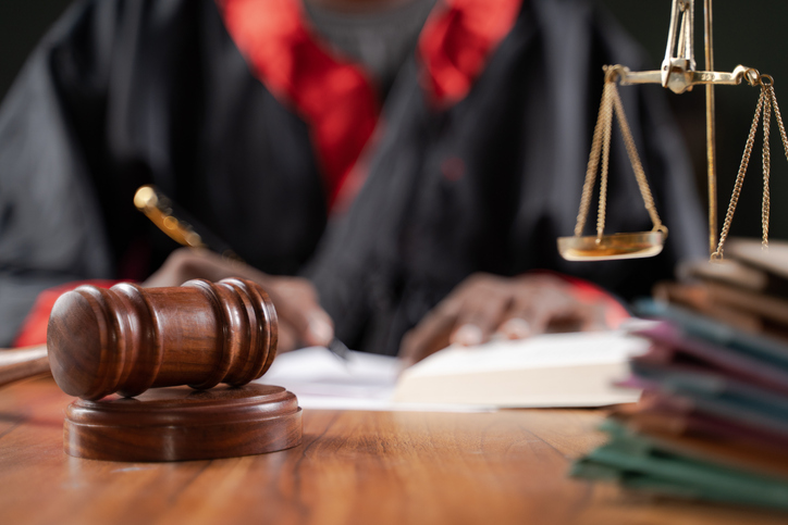Focus on judge gavel, Unrecognizable judge busy writing verdict or making notes from the book with gavel and balance scale on table.