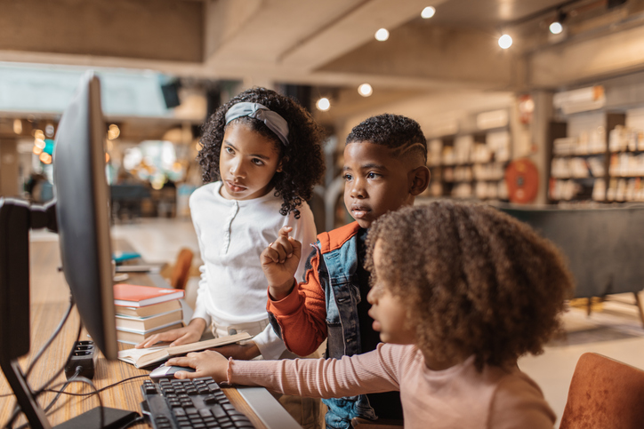 Three young black readers using a computer in a library
