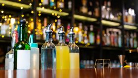 Professional bartender preparing alcoholic cocktail serving to customers at bar.