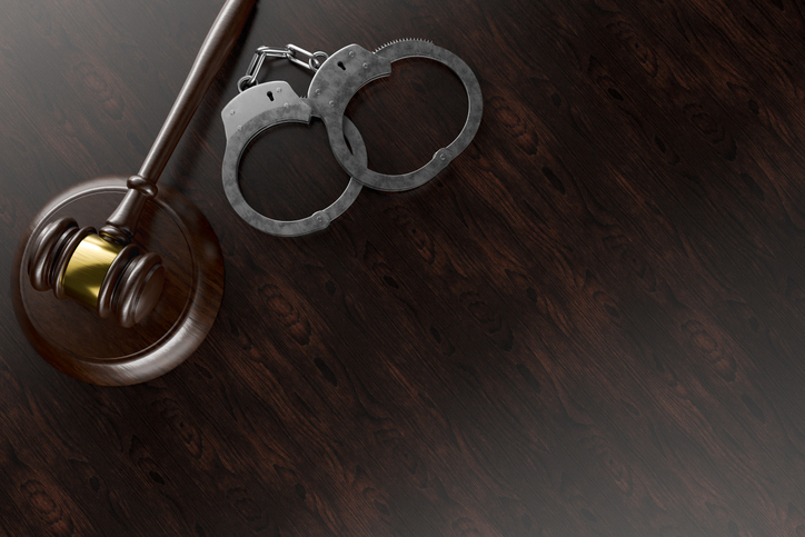 Gavel and Handcuffs on a Wooden Desk or Table Surface with Room for Copy.