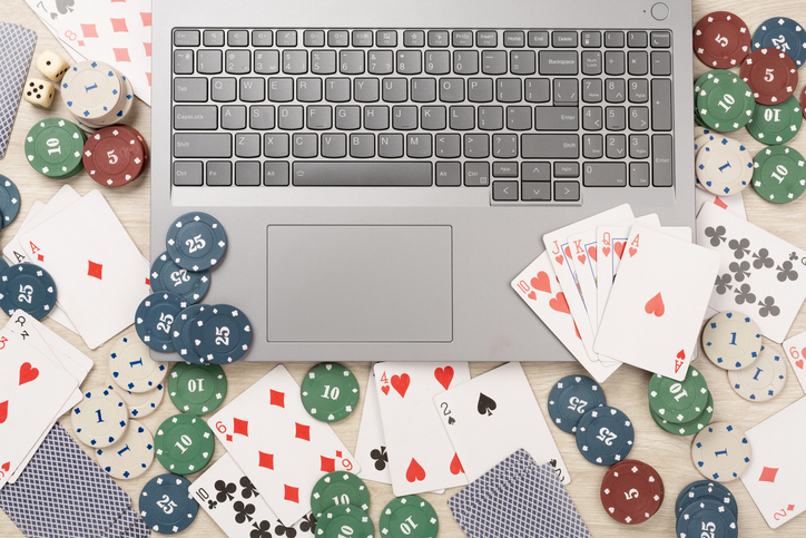 Poker chips and playing cards with laptop on wooden background, top view