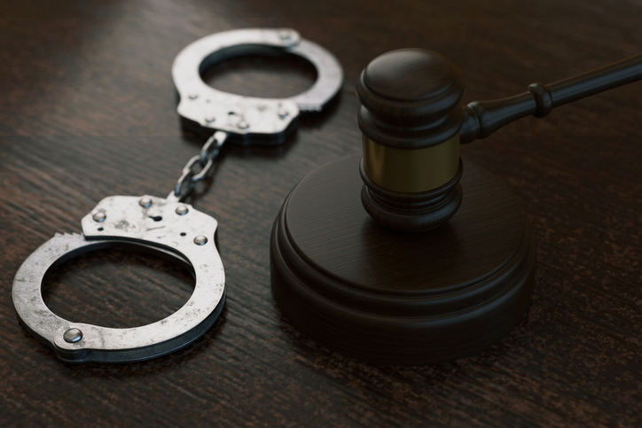 Wooden judge gavel with metal handcuffs on a dark table. Concept of criminal law, arrest, punishment, and justice system. Professional legal background for courtroom and crime-related themes.