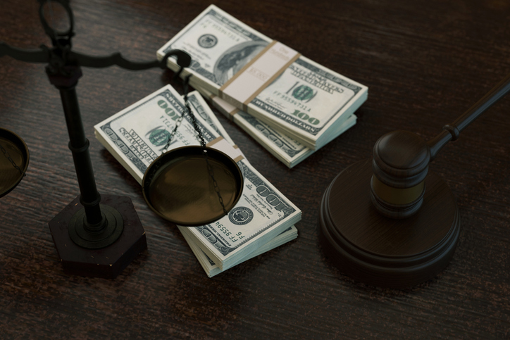 powerful conceptual shot featuring stacks of US hundred dollar bills balanced on legal scales next to a wooden judges gavel. Represents legal costs, corruption, bribery, and financial justice. Law