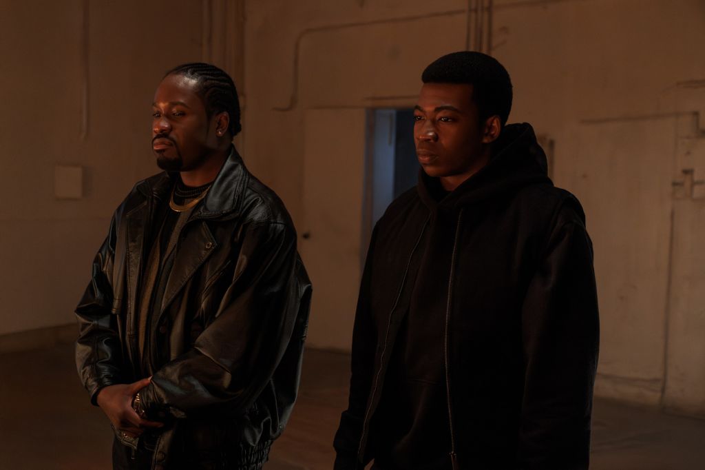 Two men in black jackets standing in a dimly lit room.