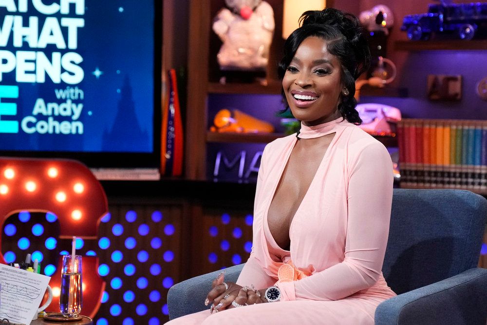 A smiling woman wearing a pink outfit sitting on a couch in front of a "Watch What Happens Live with Andy Cohen" backdrop.
