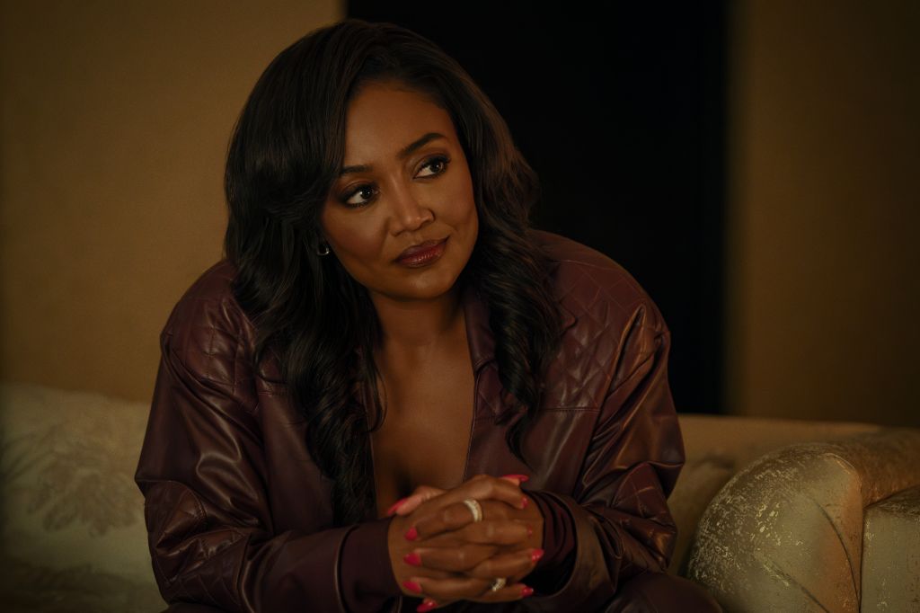 A woman with long dark hair wearing a burgundy leather jacket sits on a couch, looking thoughtfully at the camera.