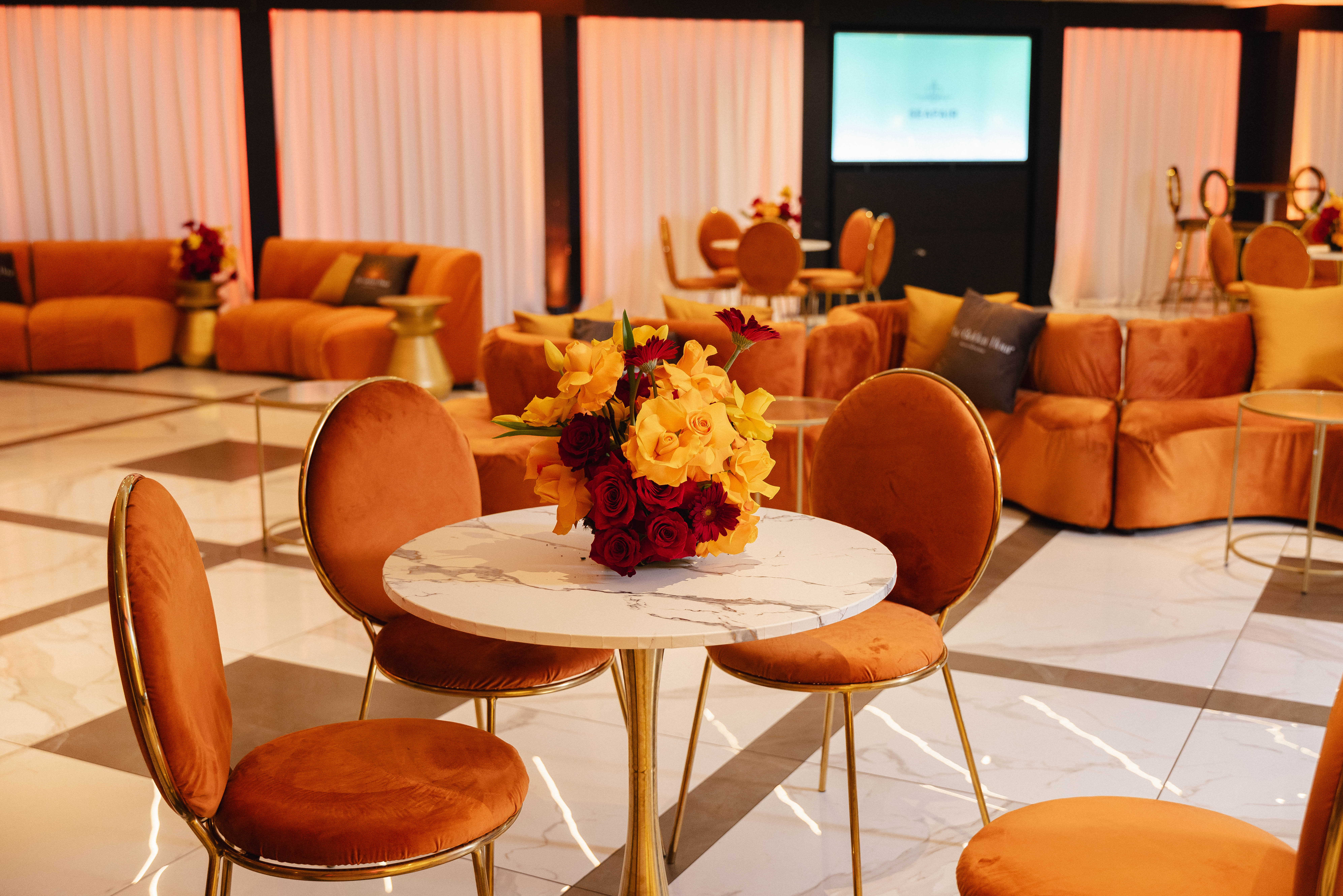A cozy lounge area with plush orange chairs and a marble-topped table with a colorful floral arrangement.