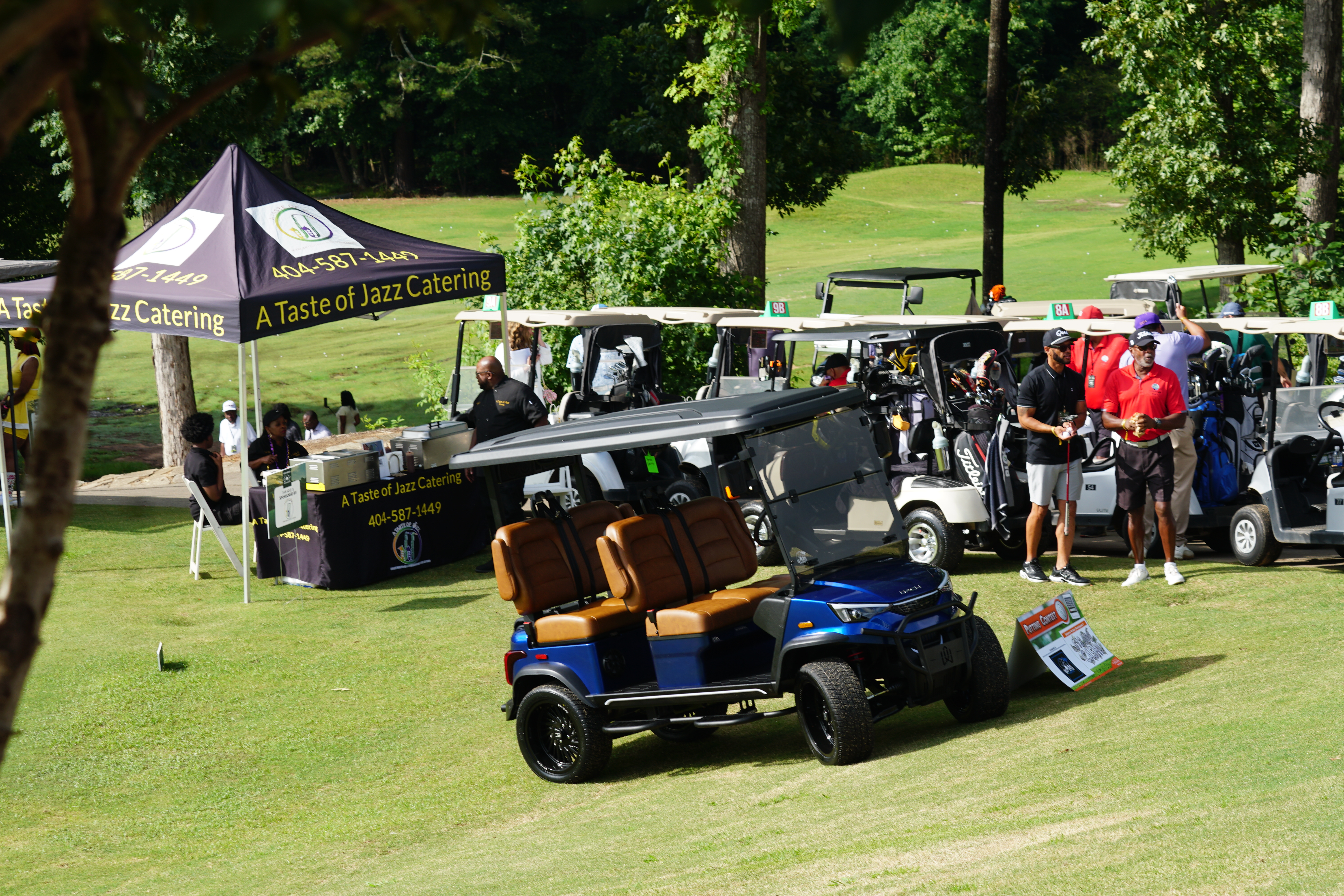 A Taste of Jazz Catering food truck and golf carts on a grassy golf course surrounded by trees.