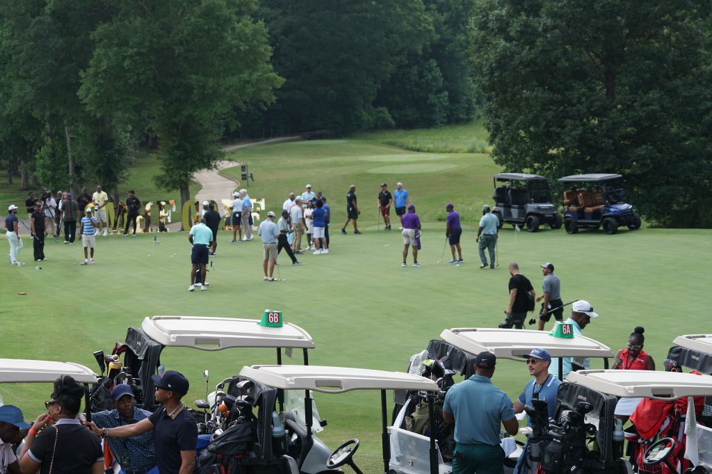 A golf course with a group of people playing on the green, surrounded by golf carts and spectators.