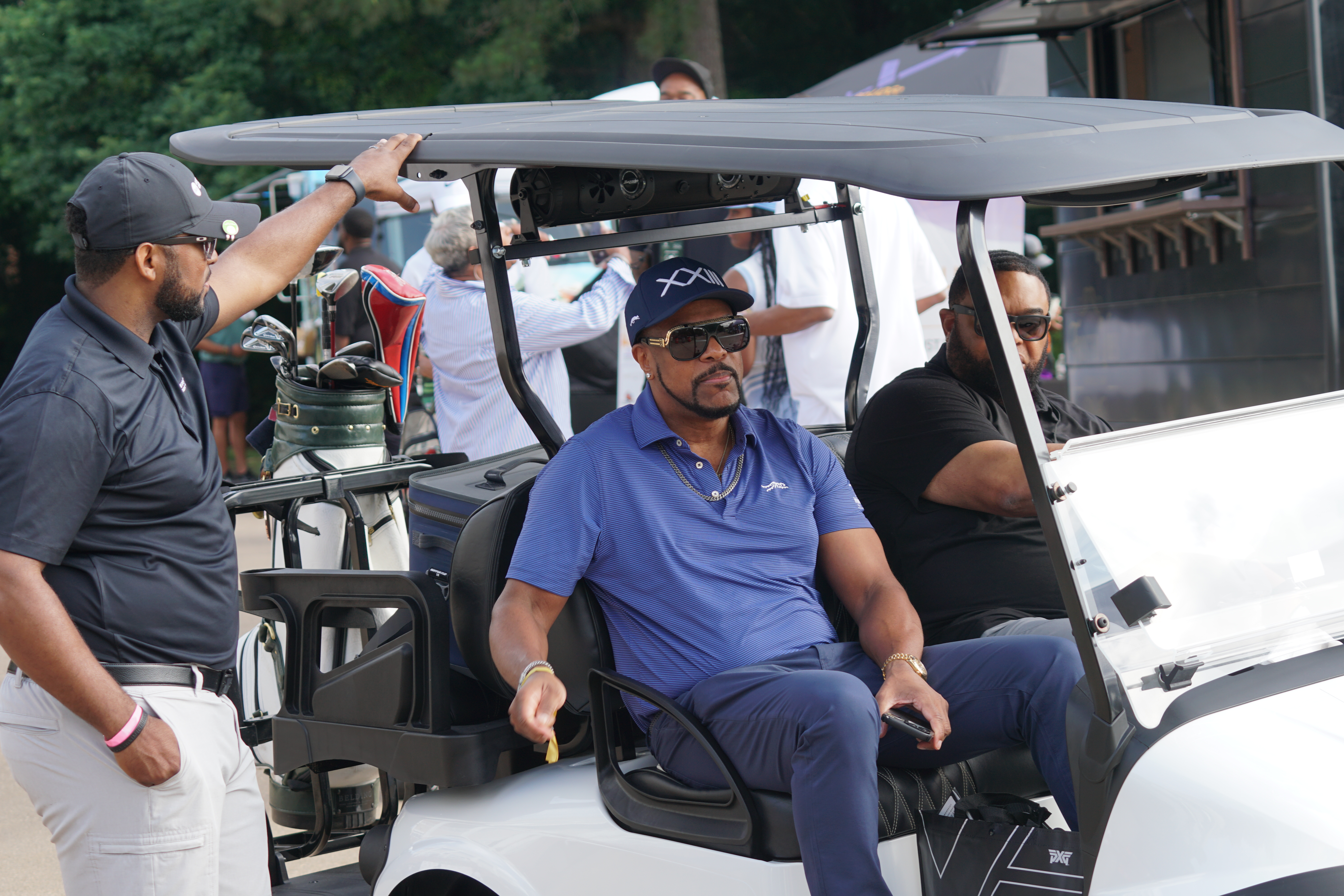 A group of people, including a man wearing a blue polo shirt, sitting in a golf cart on a golf course.