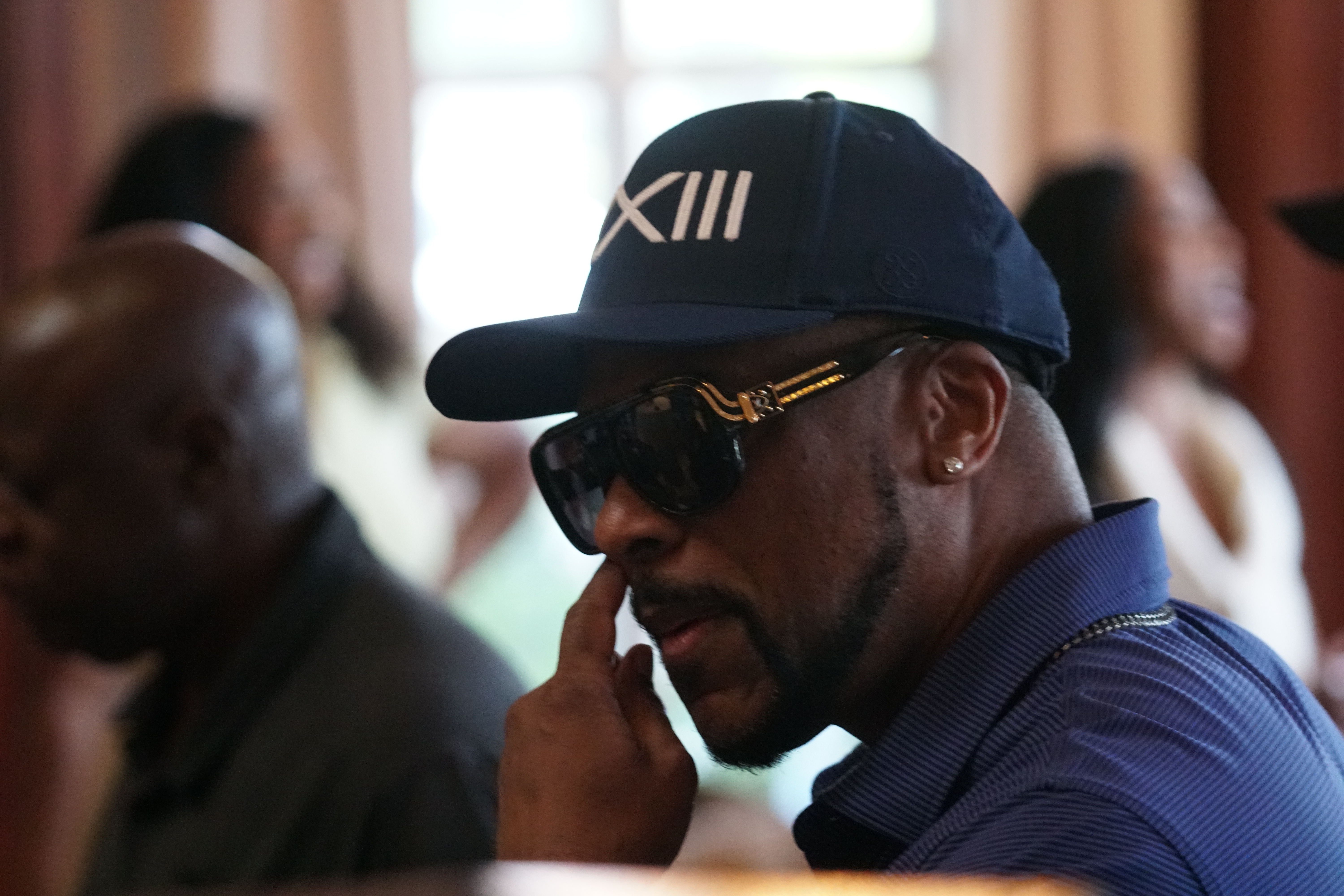 A man wearing a black hat with the text "XIII" on it, speaking on a mobile phone.