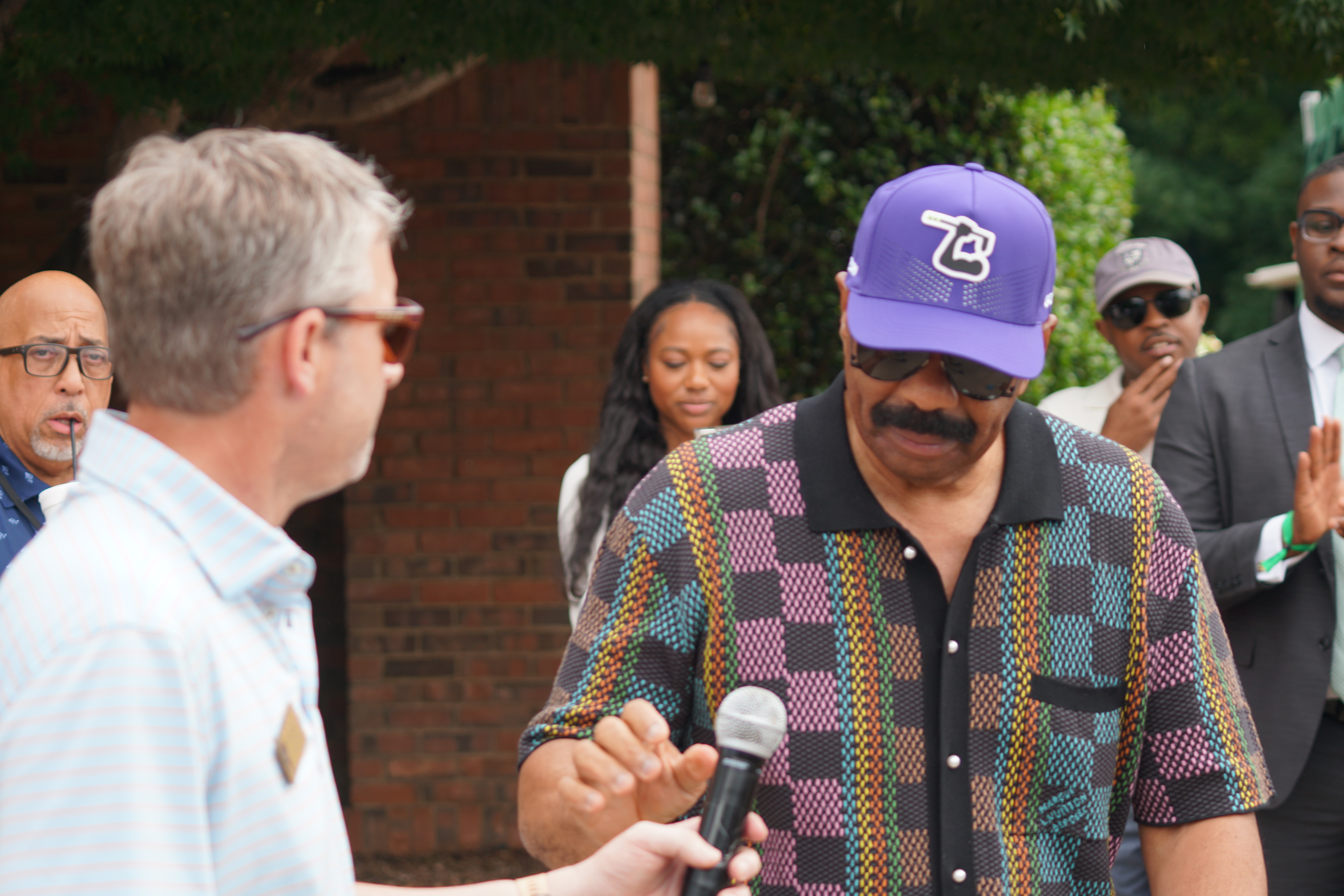 A group of people, including a man wearing a purple baseball cap with "ZB" logo, being interviewed outdoors.