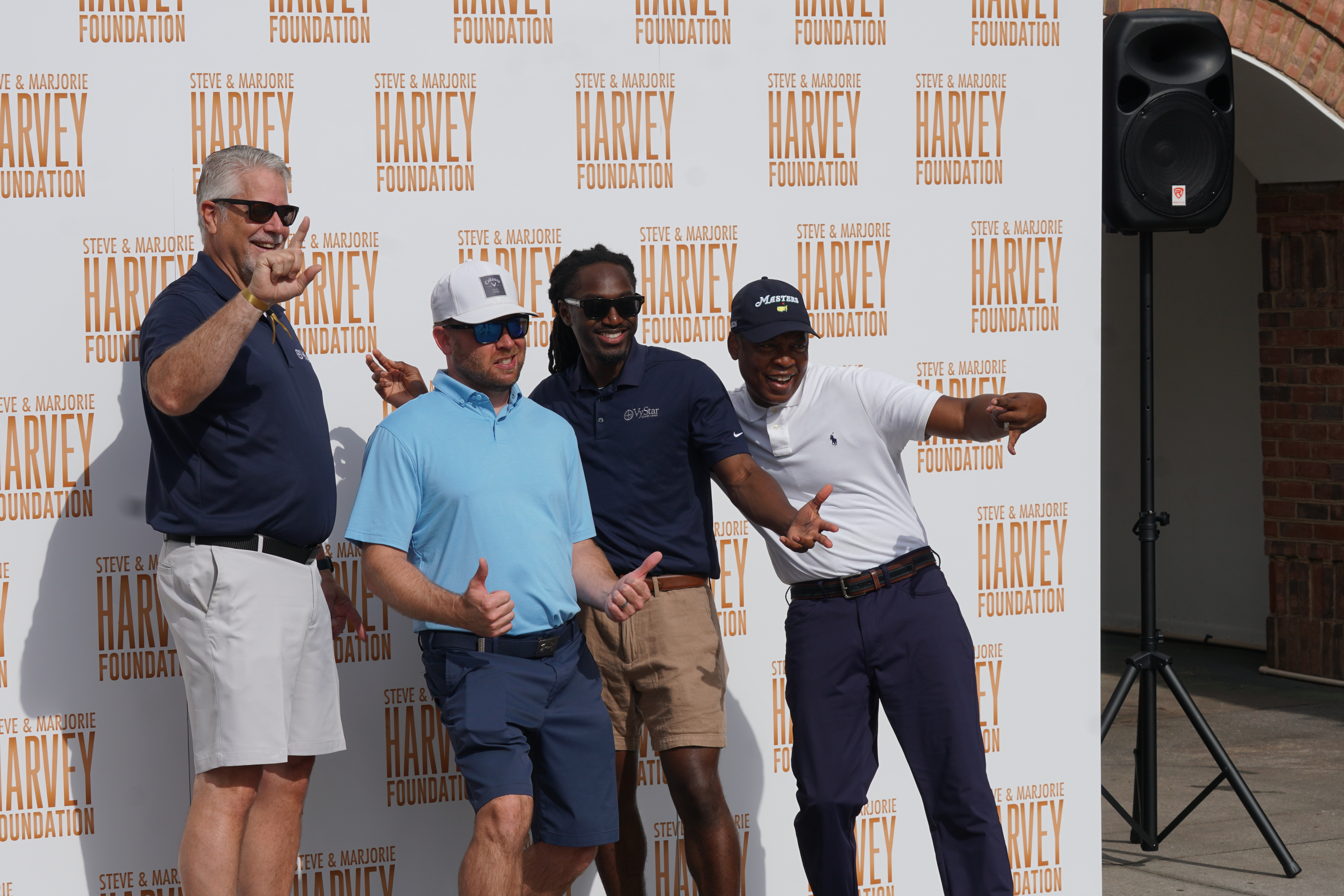 A group of men posing in front of a backdrop with the "Steve & Marjorie Harvey Foundation" logo.