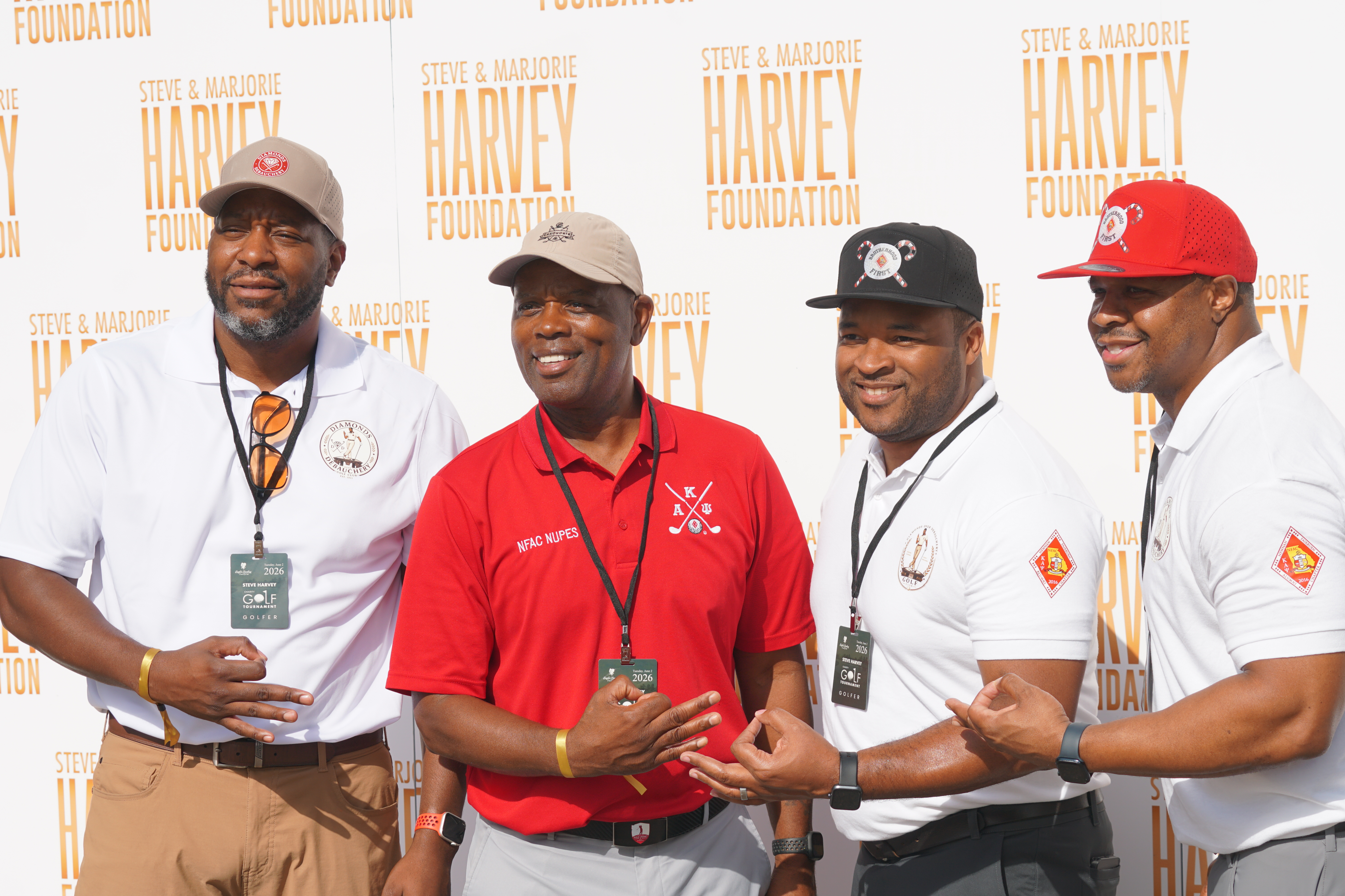 A group of men wearing uniforms and hats with the Steve & Marjorie Harvey Foundation logo, standing together and smiling.