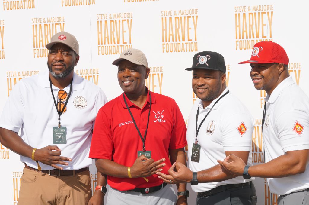 A group of men wearing uniforms and hats with the Steve & Marjorie Harvey Foundation logo, standing together and smiling.