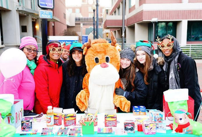 A group of people wearing winter clothing and costumes posing with a large stuffed animal in front of a city street.