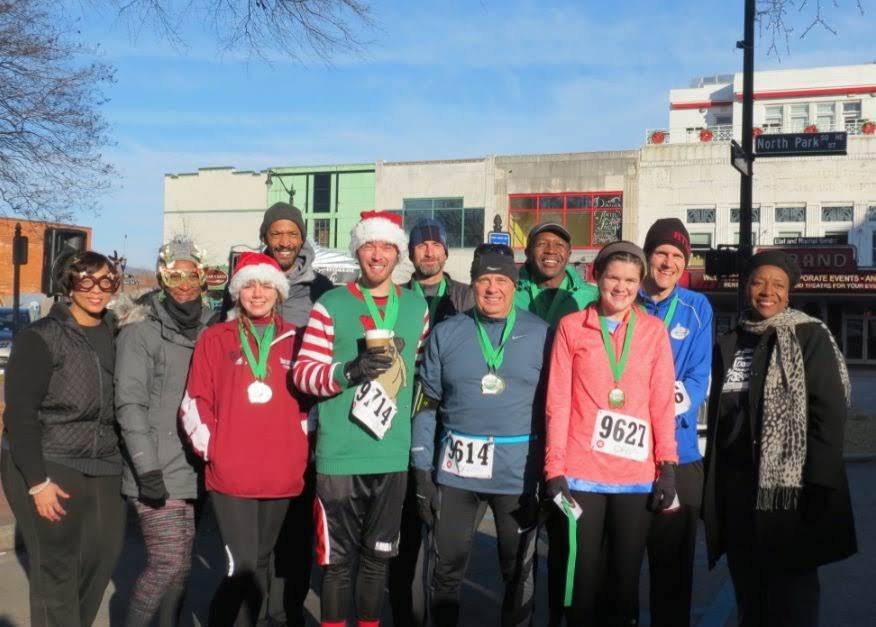 A group of people wearing holiday-themed clothing and medals, posing together outdoors in front of a building.