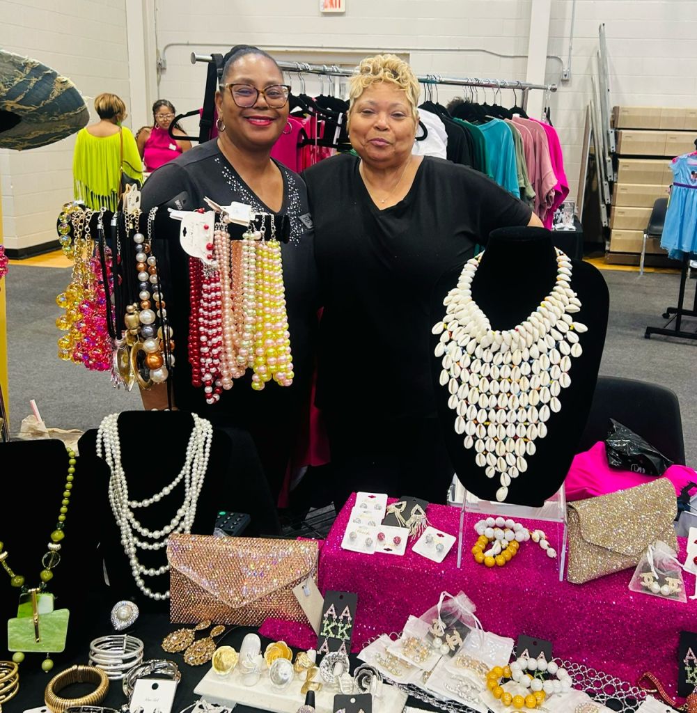 Two women standing in front of a display of colorful jewelry and accessories, including necklaces, bracelets, and earrings.