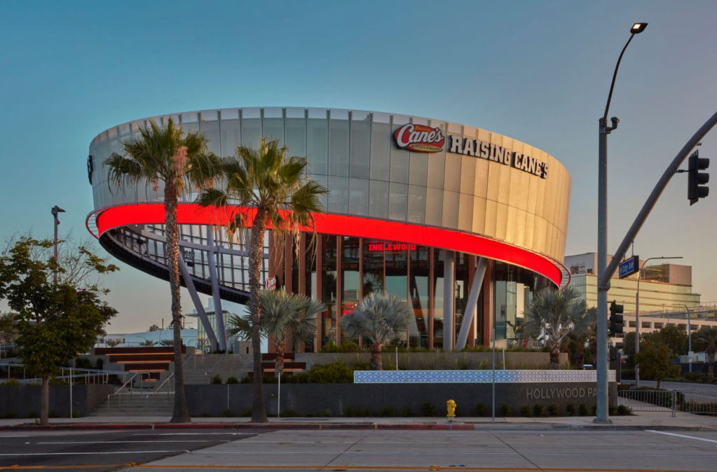 Canes Raising Cane's restaurant building with palm trees and Hollywood Park sign in foreground.