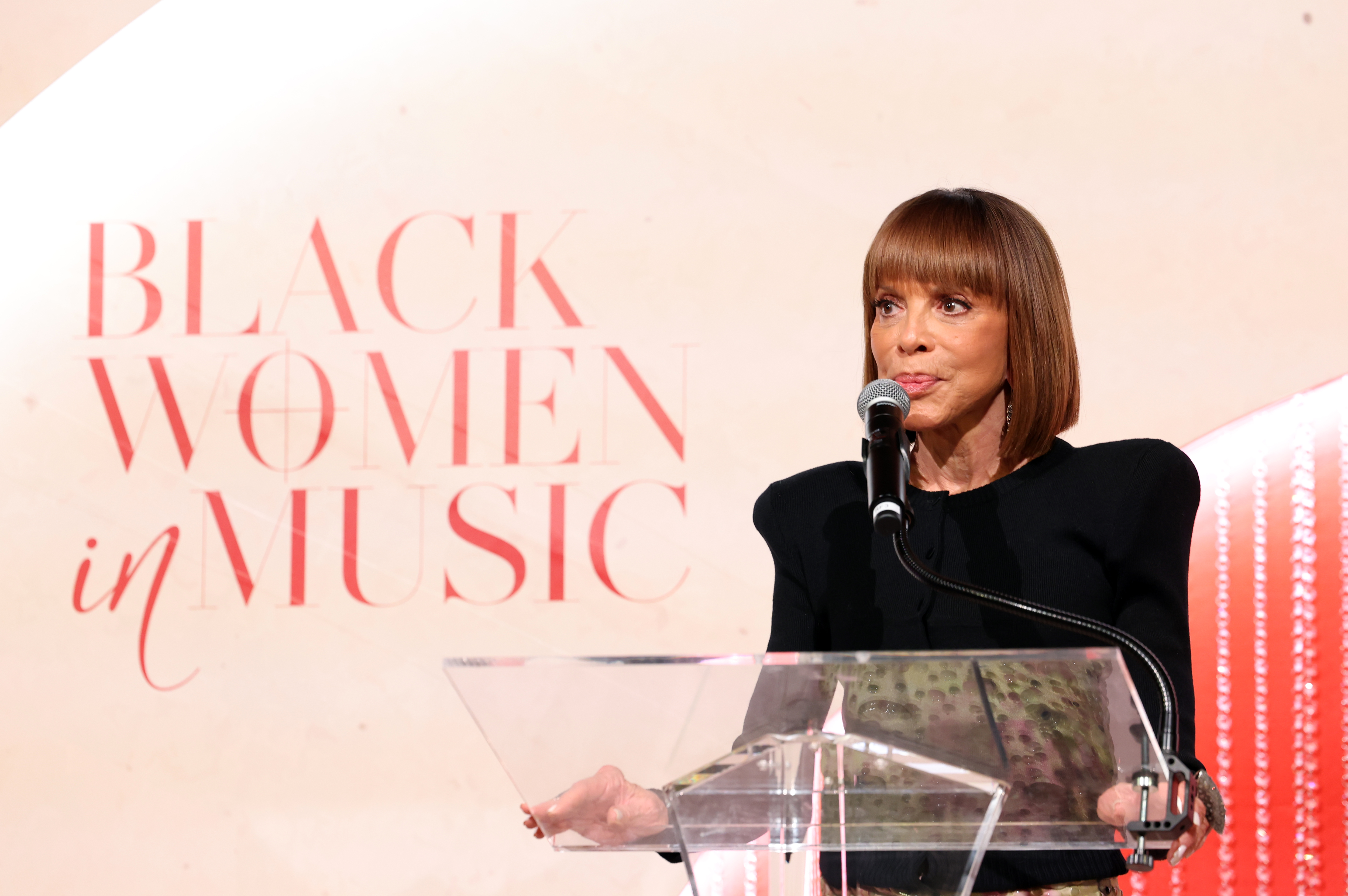 A woman speaking at a podium with the text "Black Women in Music" displayed behind her.