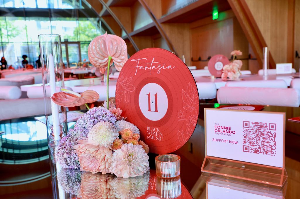 A festive event space with pink and white floral arrangements, a large red circular display with the text "Fantasia 11", and a QR code for the Connie Orlando Foundation.