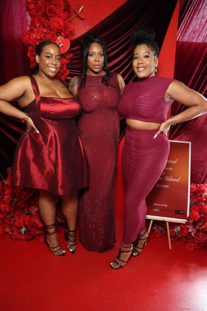 Three women in red dresses posing in front of a red floral backdrop with a sign that says