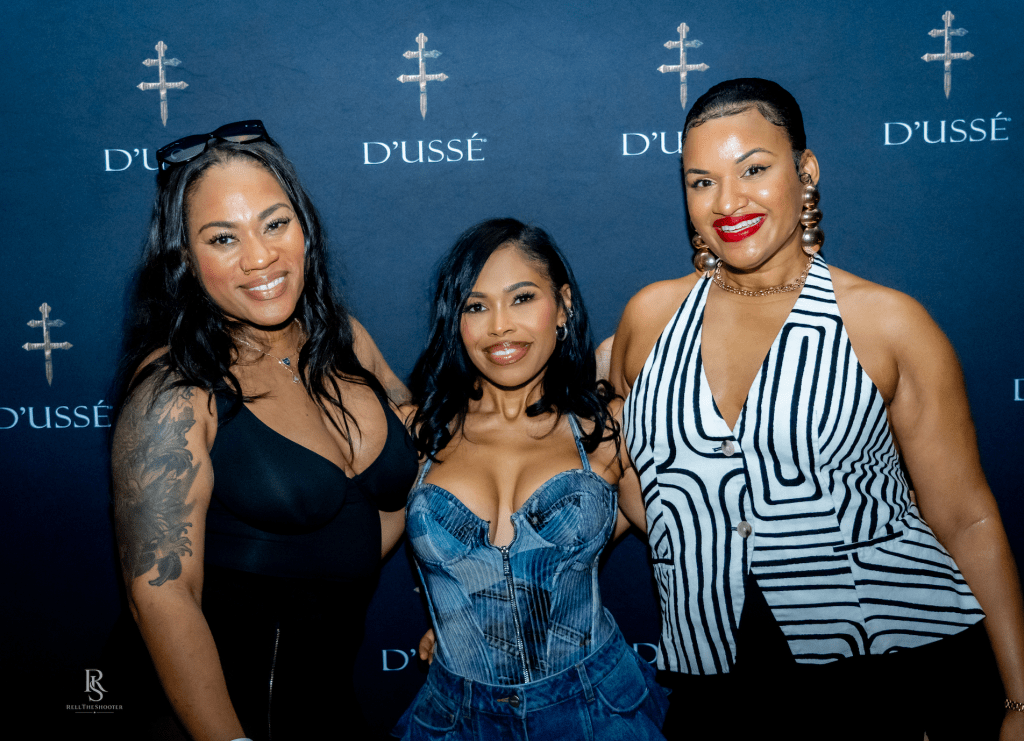 Three women posing in front of a D'usse backdrop, wearing stylish outfits with bold patterns and colors.