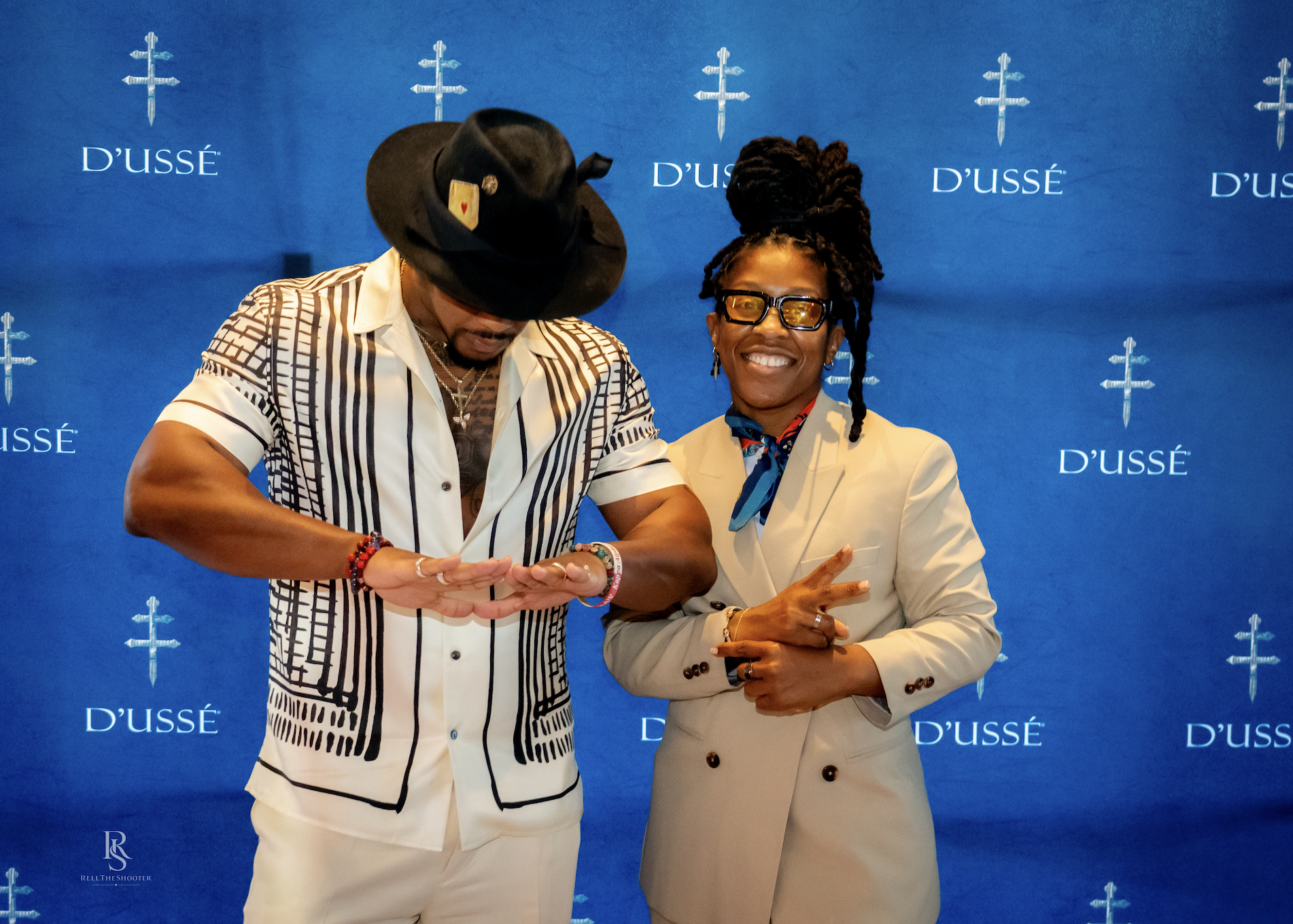 Two people in formal attire shaking hands in front of a blue backdrop with the "D'usse" logo.