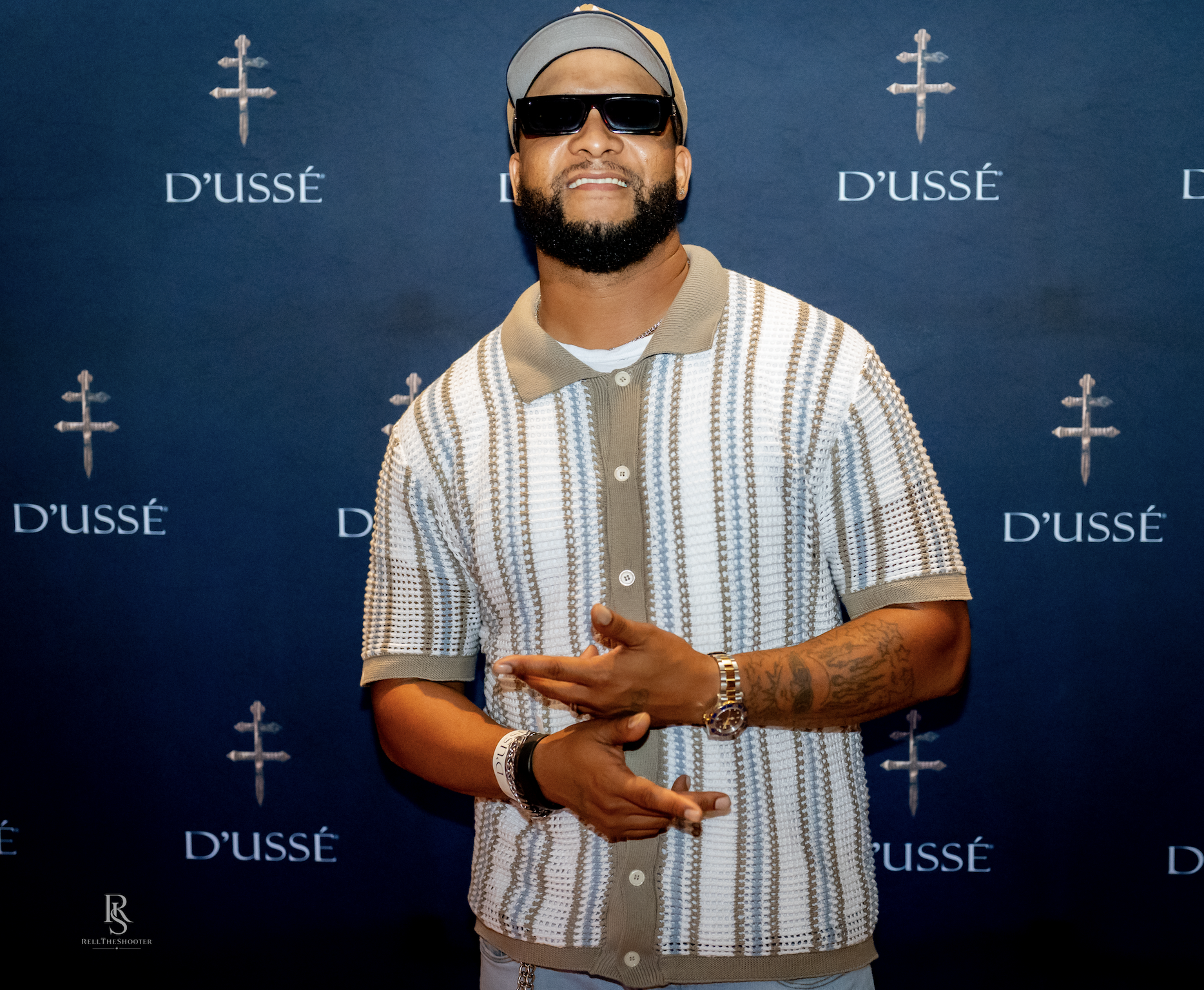 A man wearing sunglasses and a striped shirt stands in front of a backdrop with the "D'USSE" logo.