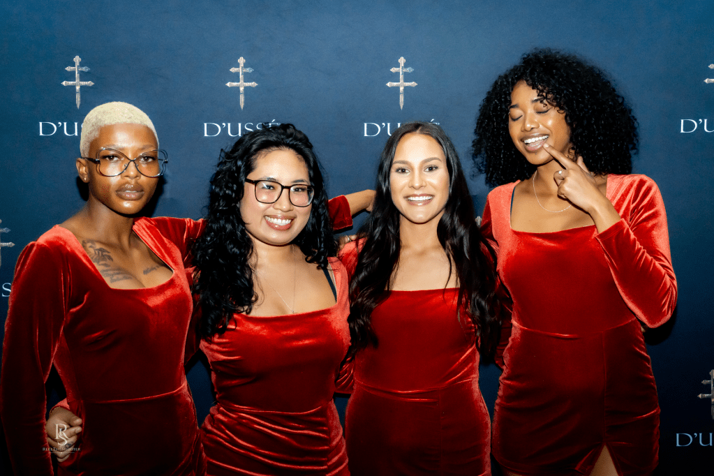 Four women in red velvet dresses posing in front of a D'usse backdrop.