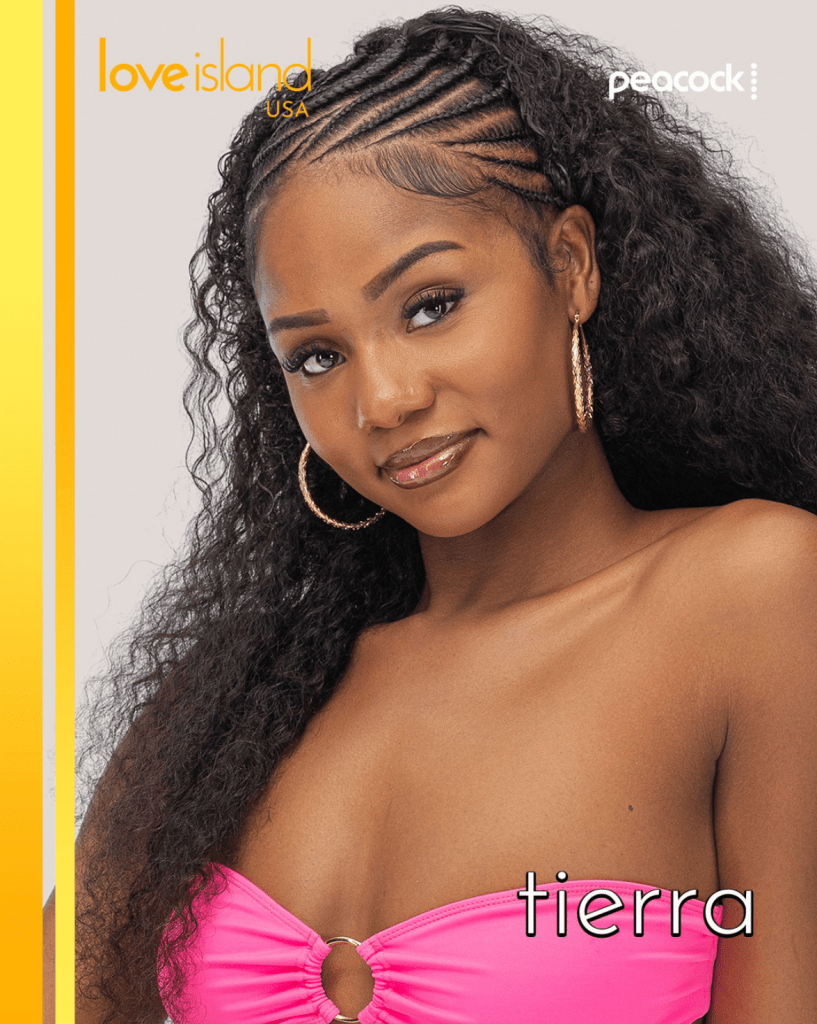 A woman with long, curly dark hair wearing a pink bikini top and gold hoop earrings. The text "love island USA" and "Peacock" are visible.