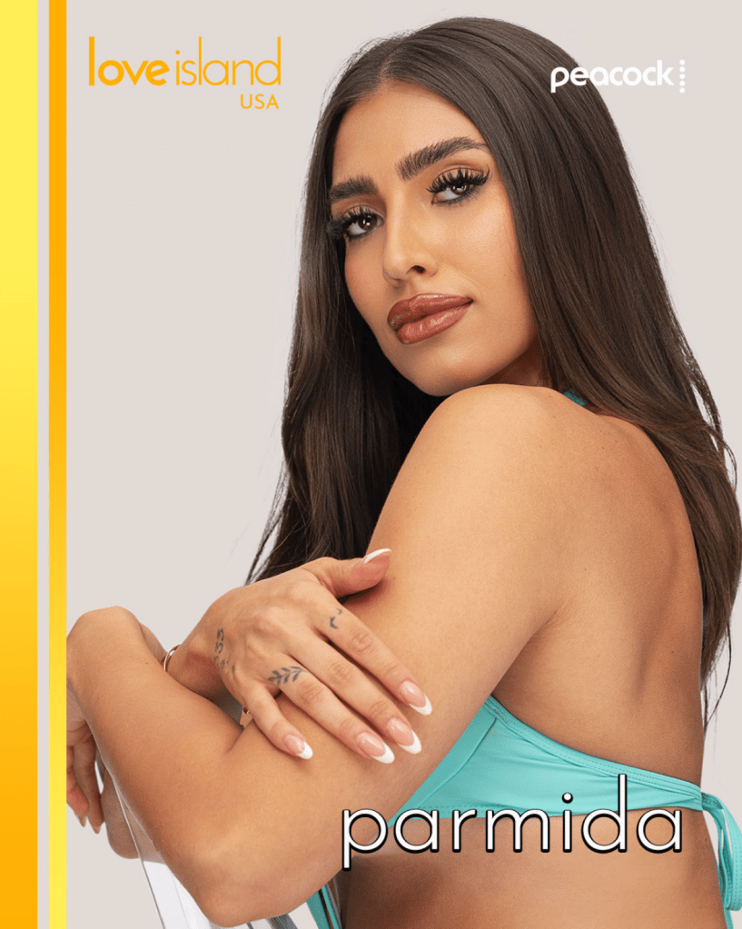 A woman with long dark hair wearing a teal top poses for a photo, with the "Love Island USA" logo visible in the background.