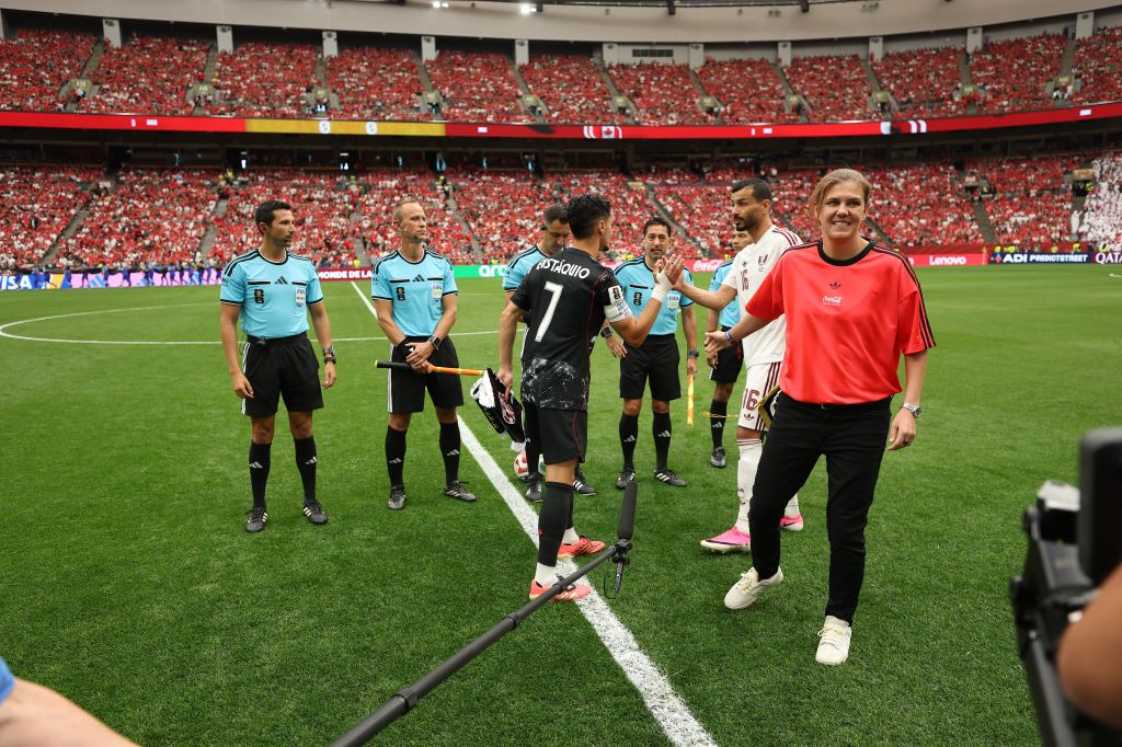 Soccer players and referees on the field before a match, with a large crowd in the stadium stands.