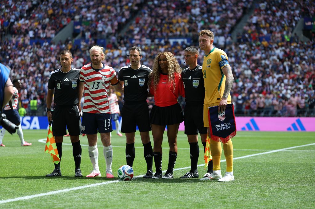 A group of soccer players, including the United States and Australian national teams, standing on a field before a match. The players are wearing their respective team uniforms and the field is surrounded by a large crowd.