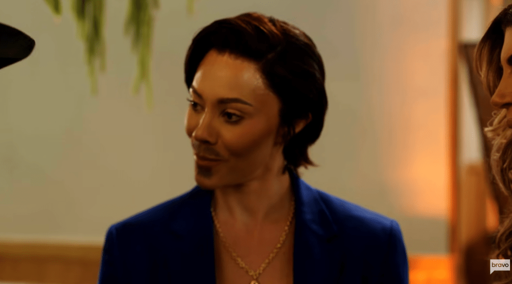 A person with dark hair wearing a blue jacket looking thoughtfully at the camera.