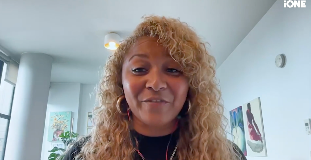 A middle-aged woman with curly blonde hair and large hoop earrings smiling at the camera.