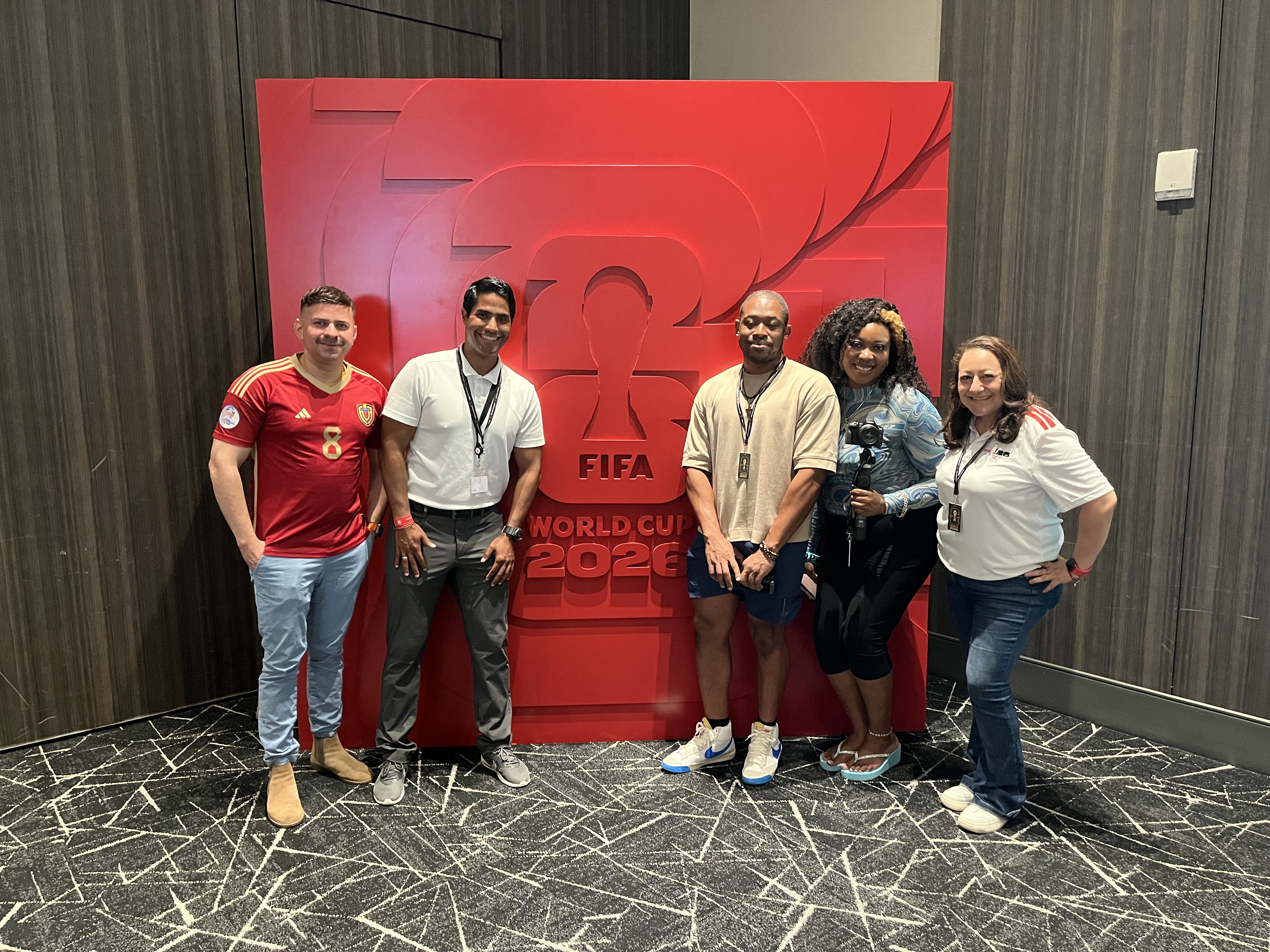 A group of 5 people posing in front of a large red FIFA World Cup 2022 logo.
