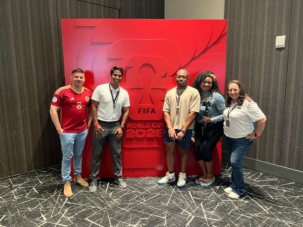 A group of 5 people posing in front of a large red FIFA World Cup 2022 logo.