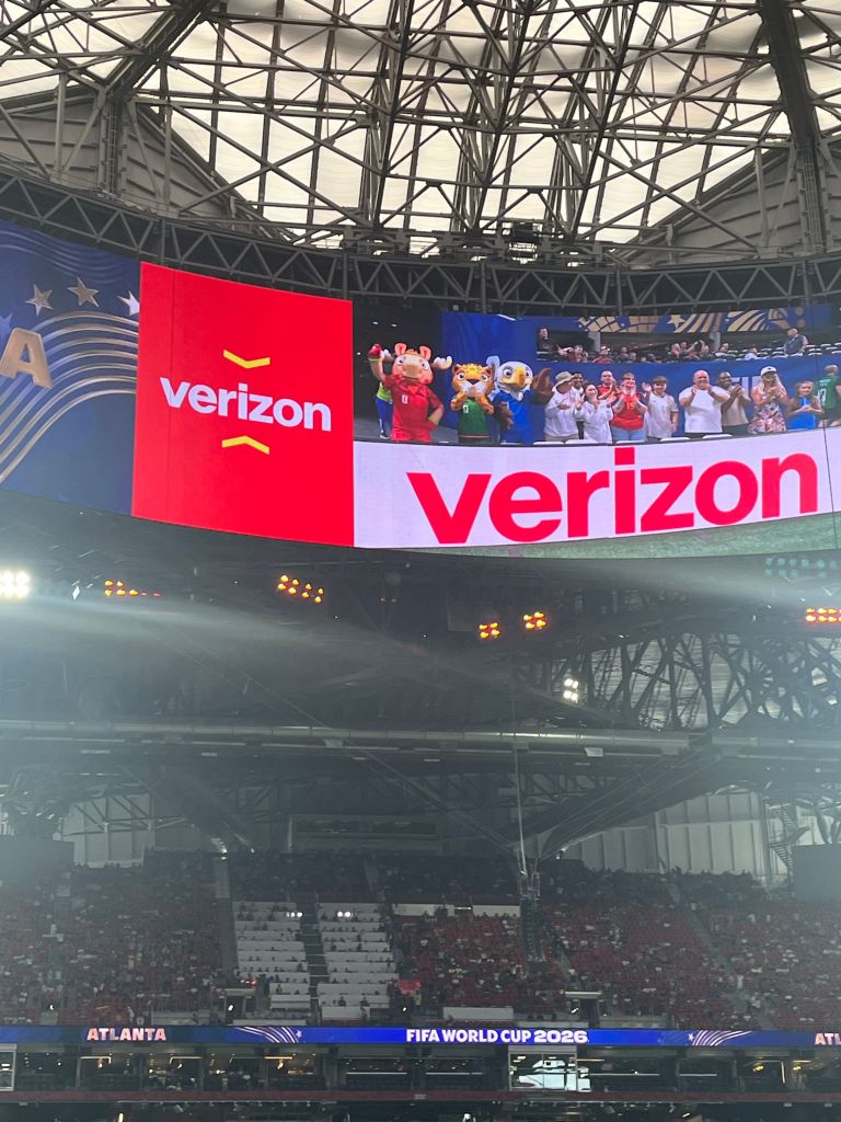 Large indoor arena with Verizon branding and mascots on the field during the 2026 FIFA World Cup event in Atlanta.