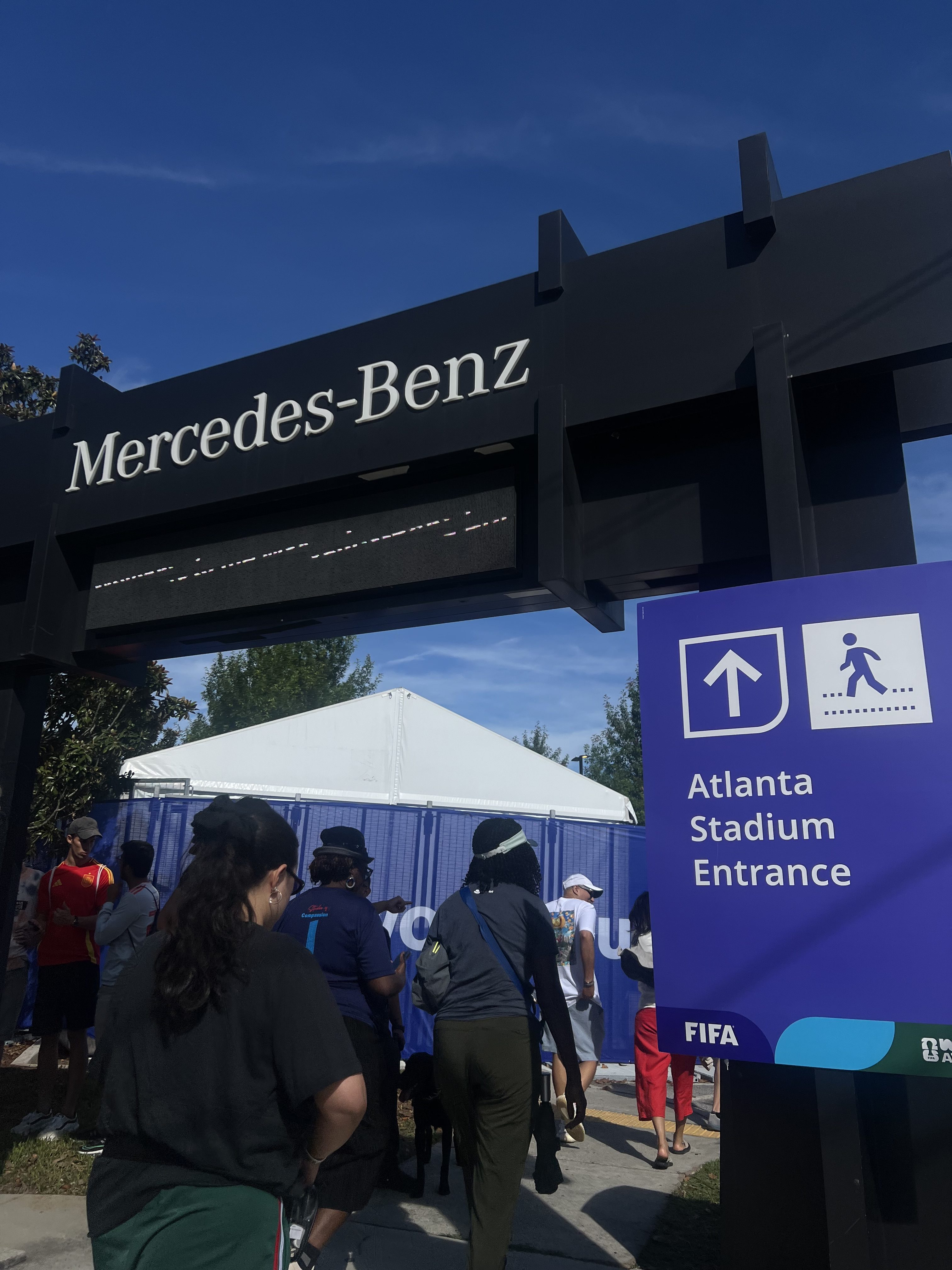 Mercedes-Benz sign above entrance to Atlanta Stadium, with people walking towards the entrance.