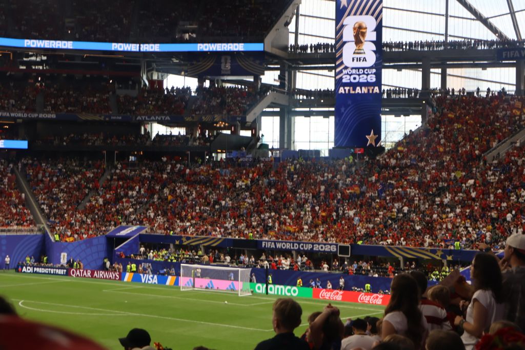 A crowded soccer stadium during the 2026 FIFA World Cup in Atlanta, with the FIFA World Cup trophy and branding visible.