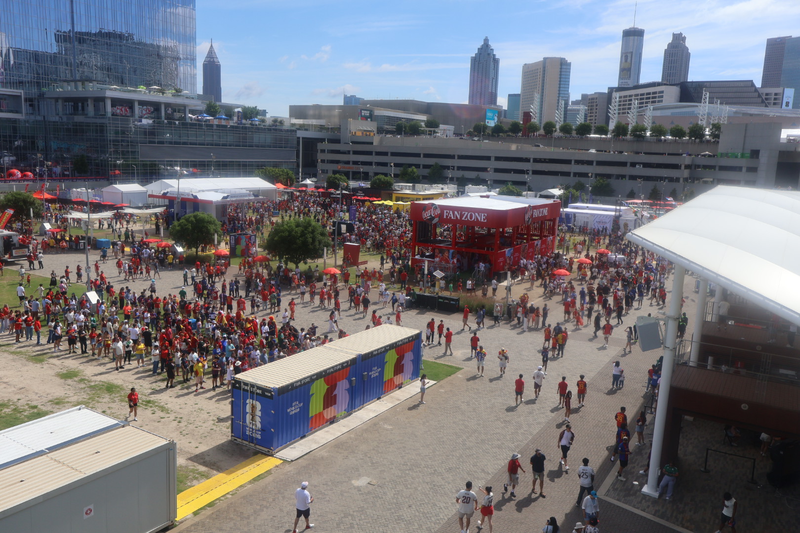Crowded outdoor event with tents, food trucks, and spectators in a city skyline setting.