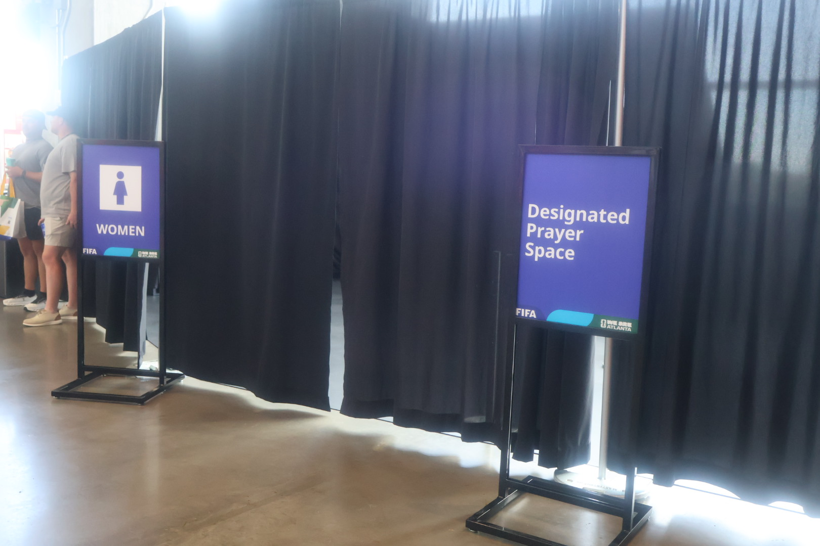 Designated Prayer Space and Women's restroom signs in a venue with black curtains and lighting.