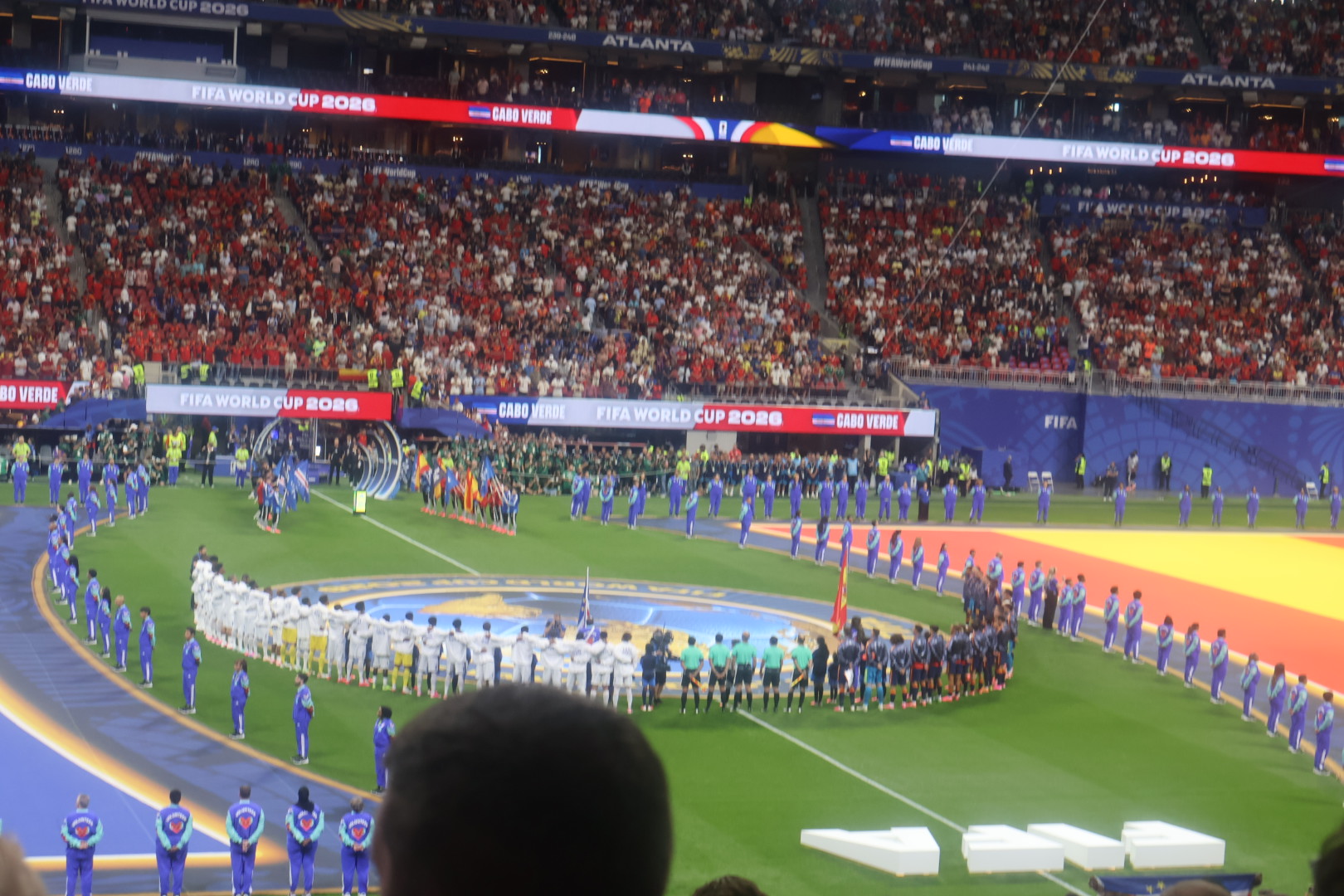A crowded soccer stadium during the FIFA World Cup, with players and officials lined up on the field and spectators filling the stands.
