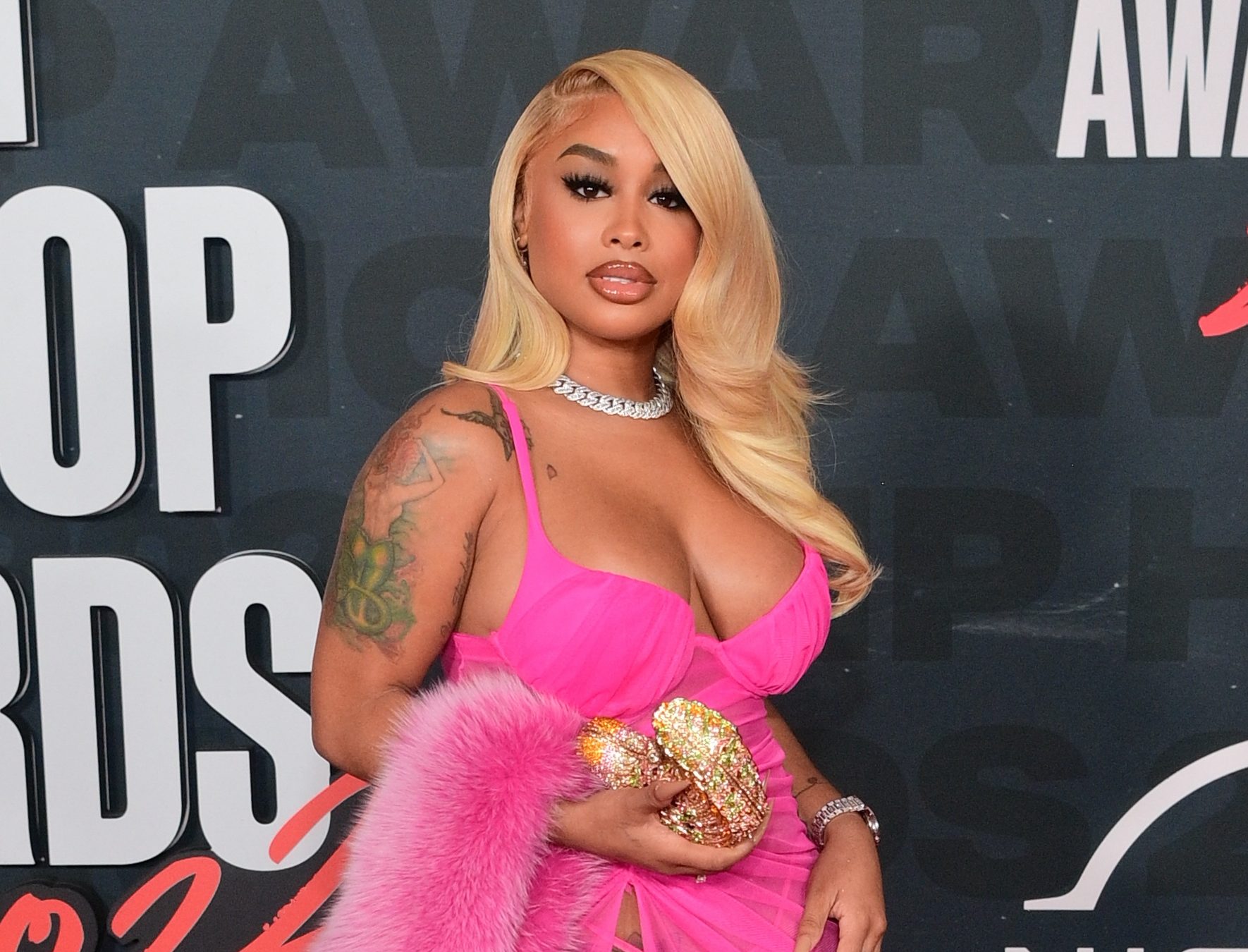 A woman with long blonde hair wearing a bright pink dress and fur coat poses on the red carpet at the BET Hip Hop Awards 2022 in Atlanta.